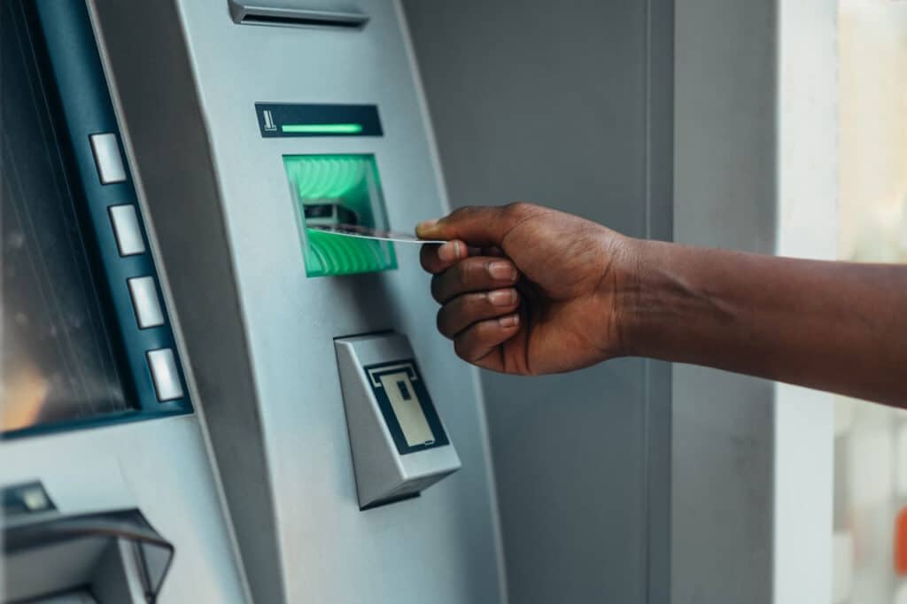Young African American woman using an atm machine and a credit card while in the city